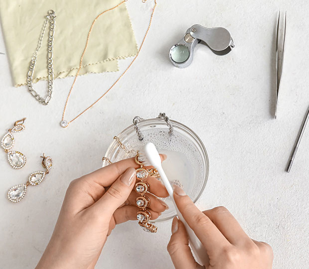 Woman's hands cleaning a piece of jewelry with multiple tools