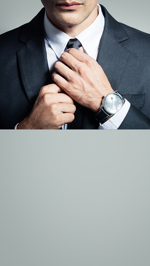 Man in black tuxedo straightening his tie. His luxury watch is peeking out of his left sleeve.