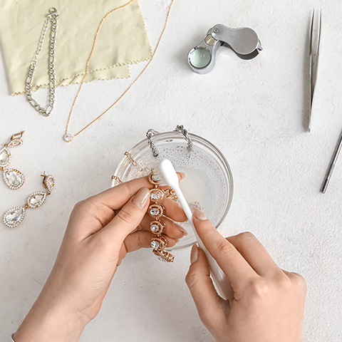 Woman's hands cleaning a piece of jewelry with multiple tools