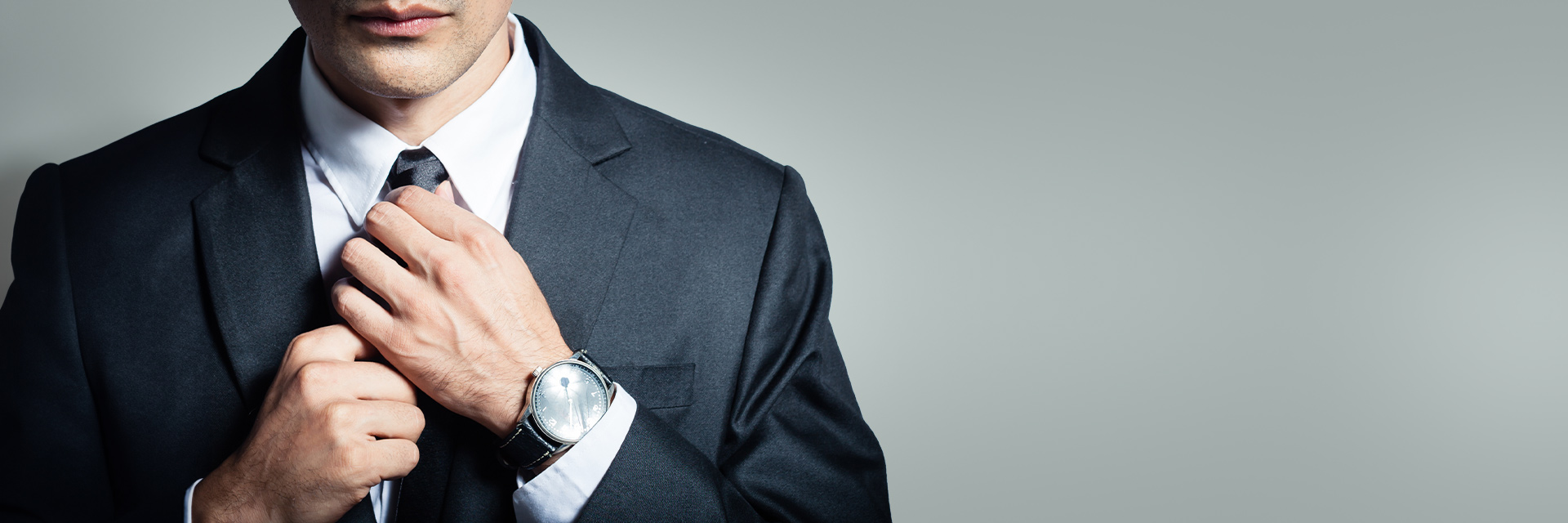 Man in black tuxedo straightening his tie. His luxury watch is peeking out of his left sleeve.