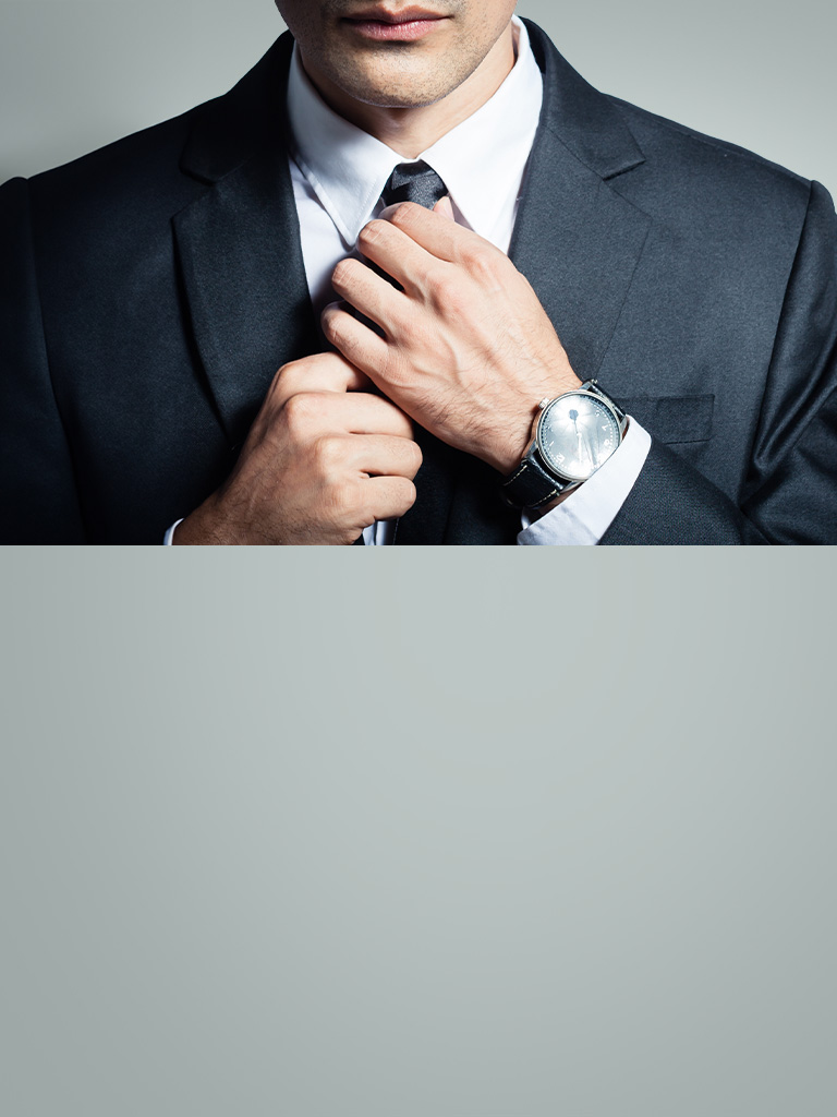 Man in black tuxedo straightening his tie. His luxury watch is peeking out of his left sleeve.