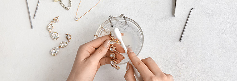 Woman's hands cleaning a piece of jewelry with multiple tools